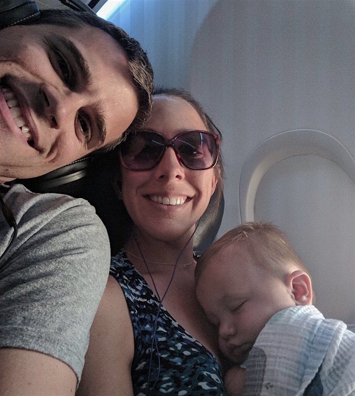 Me and my husband with baby sleeping on me by plane window. 
