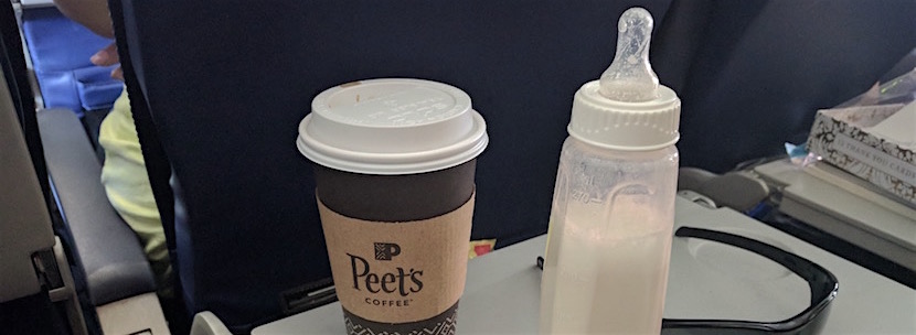 Coffee and baby bottle on airplane tray table.