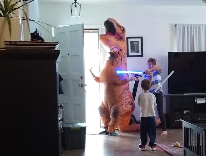 kids with toy lightsabers fighting a kid in a dinosaur costume
